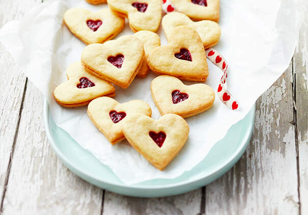 Herzförmige Linzer Kekse mit Marmelade liegen auf einem Teller.