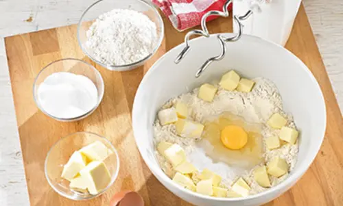 Butterwürfel, eine Ei, Mehl und Zucker sind in einer Schale.