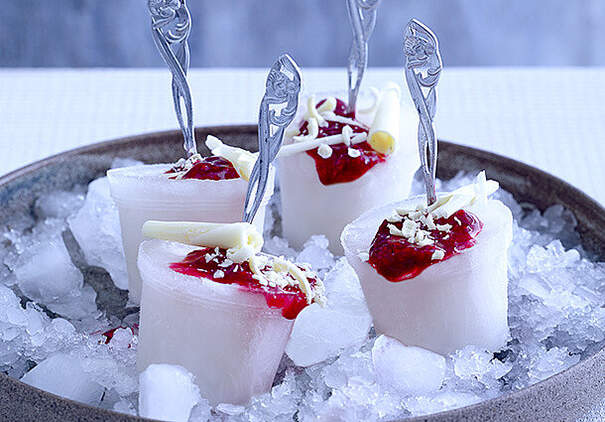 In einer Schale mit Crushed Ice stehen kleine Sektsorbeets mit Himbeersauce. Verziert sind sie mit weißen Schokosplittern. 