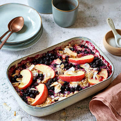 Ein Auflauf mit Apfel‑Beeren‑Crumble in einer roten Form, daneben Polaroid‑Bilder von Rezepten.