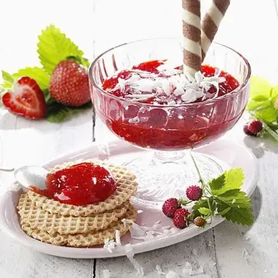 In einem flachen Eisbecherglas ist ein roter Aufstrich mit Streuseln weißer Schokolade verziert. 