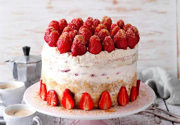 Eine kleine Torte aus dunklem Espresso‑Biskuit mit heller Mascarponecreme ist mit frischen Erdbeeren und Zuckerperlen geschmückt
