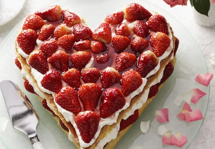 Ein herzförmiger Kuchen ist mit Quarkcreme gefüllt und mit halben Erdbeeren und Minzblättern dekoriert.