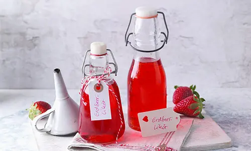 Zwei Glasflaschen mit Likör und süßen Etiketten auf dem "Erdbeer Likor" drauf steht. 
