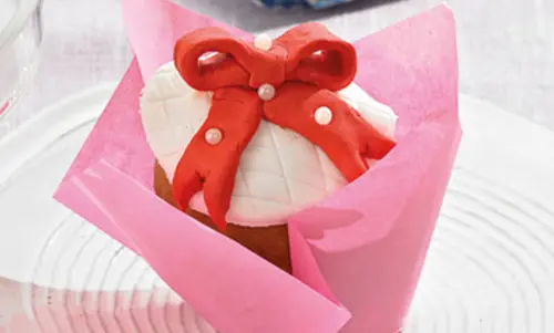 Heller Cupcake mit weißem Frosting und roter Schleife aus Fondant.