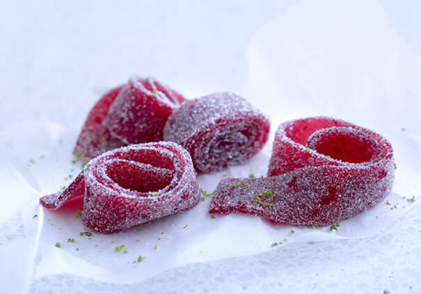 Drei rote saure Streifen liegen zusammengerollt auf einer Plastikfolie