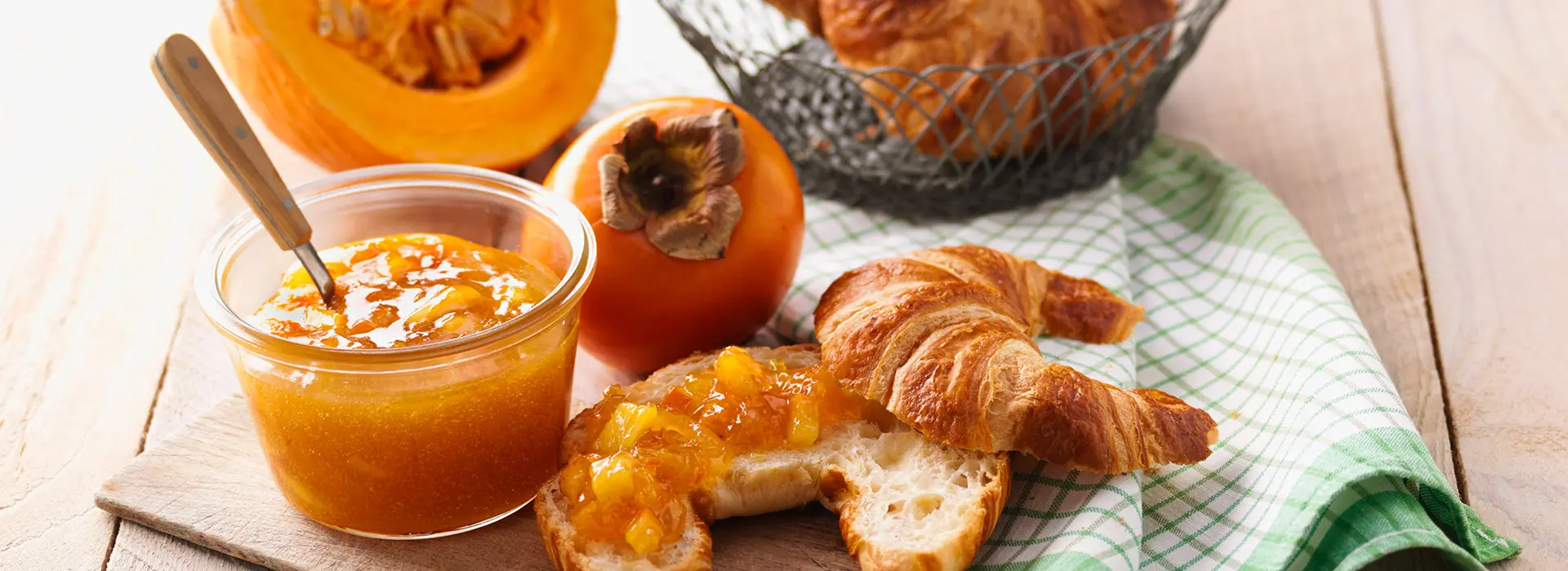 Ein Glas Kürbismarmelade steht neben einem Croissant mit Marmelade und frischen Kürbisstücken.