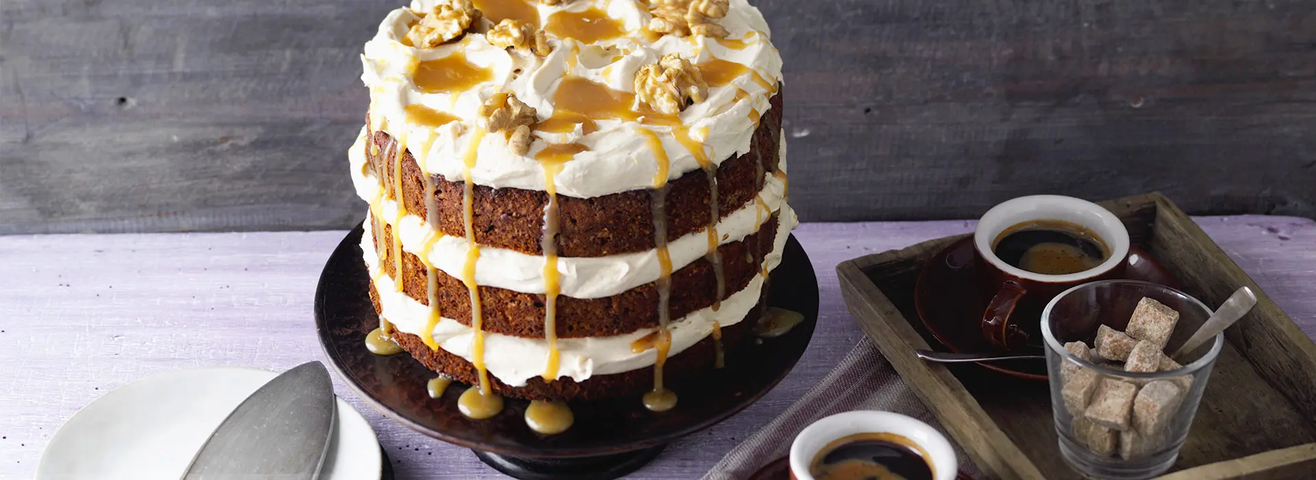 Auf einer Etagere steht eine Torte, die aus drei Böden besteht. Dazwischen ist jeweils eine Cremeschicht. Die oberste Cremeschicht ist mit Karamell und Wallnüssen verziert.