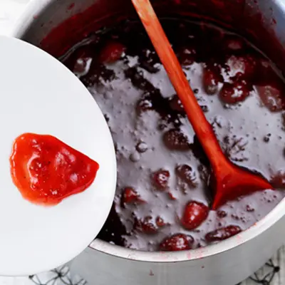 Kochtopf mit kegochten Erdbeeren, daneben ein Teller mit einem Kleck der Masse. 