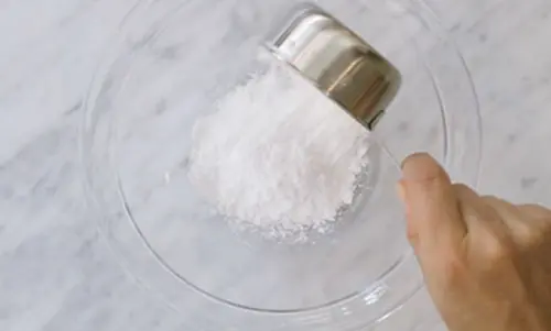 Eine Hand schüttet ein Cup Zucker in eine große Glasschale