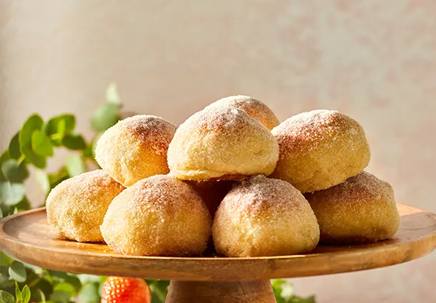Mehrere Zucker bestreute Butter‑Hefebrötchen sind auf einer Etagere gestapelt, daneben liegen frische Erdbeeren und Blätter
