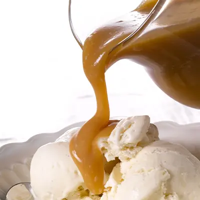 eine dickflüssige Karamellsoße wird über drei Kugeln Vanille-Eis gegossen.