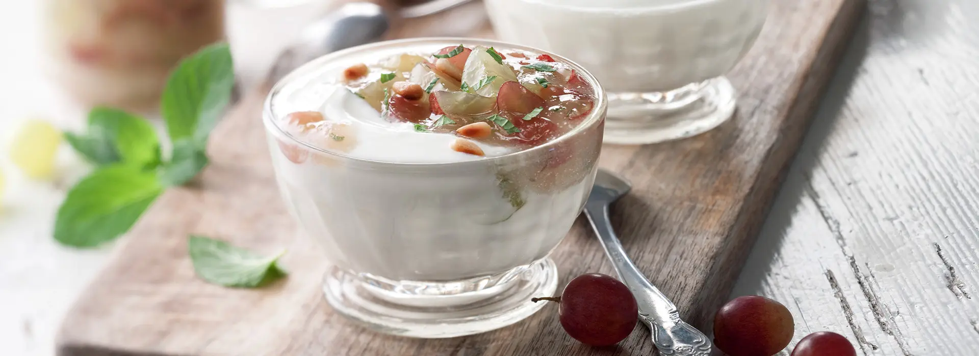 Glasschüssel auf einem Holzbrett mit einer weißen Creme aus Birnen und Äpfel, getoppt mit Trauben