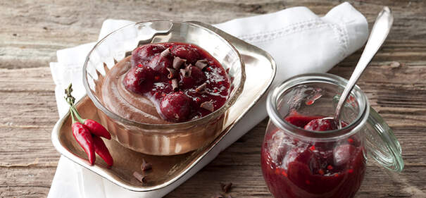In einer kleinen Schale liegt eine schokoladige Mousse, darauf sind dunkle Kirschen und geraspelte Schokolade dekoriert