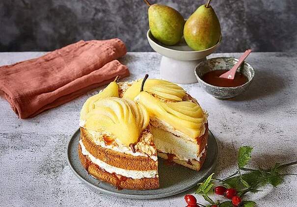 Eine Birnen-Hagebutten-Torte, geschichtet auf einem Biskuitteig. Birnen und Hagebutten sind um den Kuchen drapiert.
