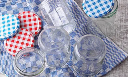 2. Gläser und Deckel Marmeladengläser liegen frisch gewaschen auf einem karierten Handtuch. Daneben liegen die rot und blauen Deckel.