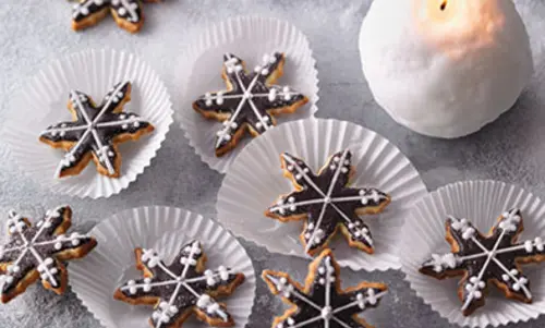 Schneeflockenförmige Kekse mit Schoko-Glasur und feinen Verzierungen aus Zuckerguss.