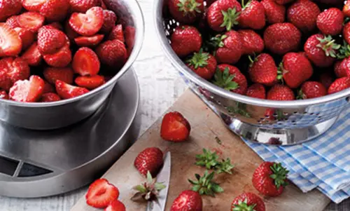 neben einer großen Wage mit geschnittenen Erdbeeren drin, steht ein großen Sieb mit unbehandelten Erdbeeren.