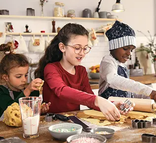 Drei Kinder backen in der Küche Weihnachtsplätzchen