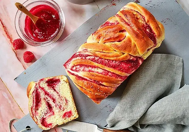 Geflochtener Hefezopf mit sichtbaren Himbeerwirbeln und goldbrauner Kruste.