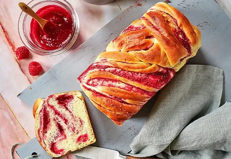 Geflochtener Hefezopf mit sichtbaren Himbeerwirbeln und goldbrauner Kruste.