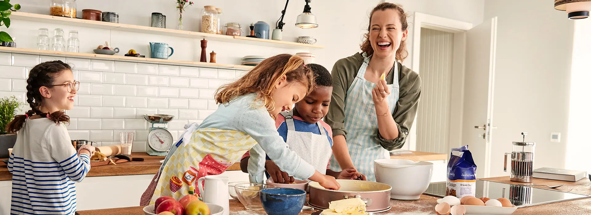 Eine Frau backt mit drei Kindern einen Kuchen. Sie freuen sich. Sie verwenden Produkte von SweetFamily