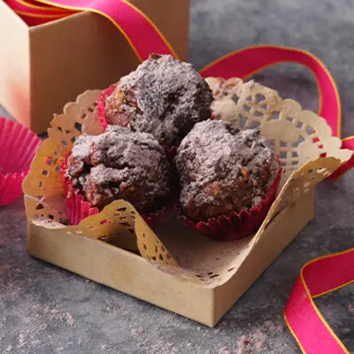 In einer braunen Muffinform liegen drei kleine Muffins mit Puderzucker verziert.