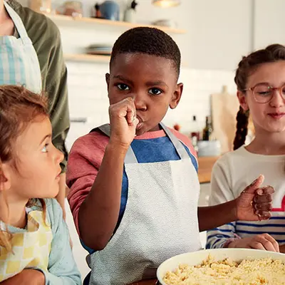 Drei Kinder die Backen, das Kind in der Mitte nascht vom Teig