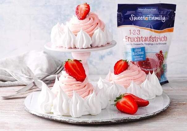 Kleine Baisertörtchen mit rosa Cremefüllung und einer Packung 1-2-3 Fruchtaufstrich von Sweet Family daneben.