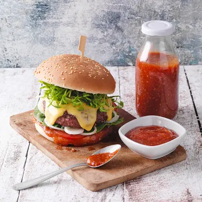 Burger auf einem Holzbrett mit einer flasche roter Grillsauce