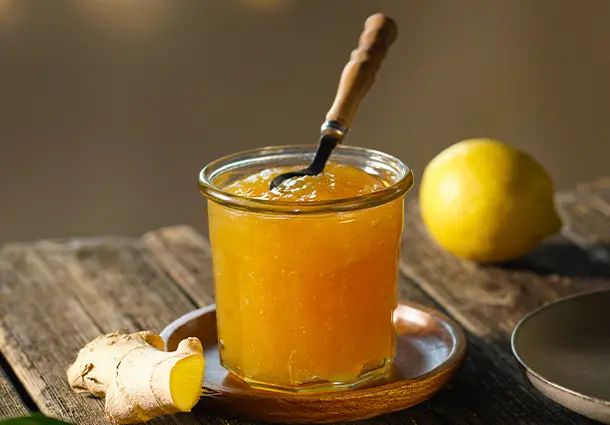 Ein Glas Zitronen-Ingwer-Marmelade steht auf einem Brett, daneben liegen Zitronen und ein Stück Ingwer