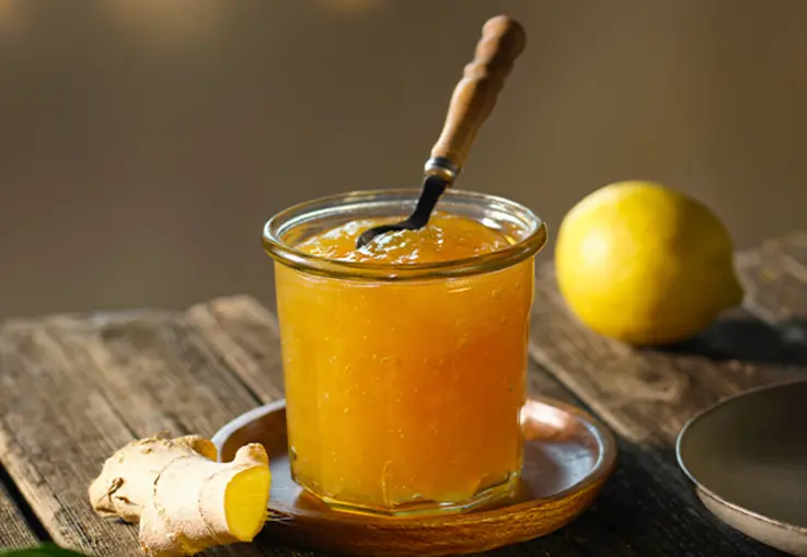Ein Glas Zitronen-Ingwer-Marmelade steht auf einem Brett, daneben liegen Zitronen und ein Stück Ingwer