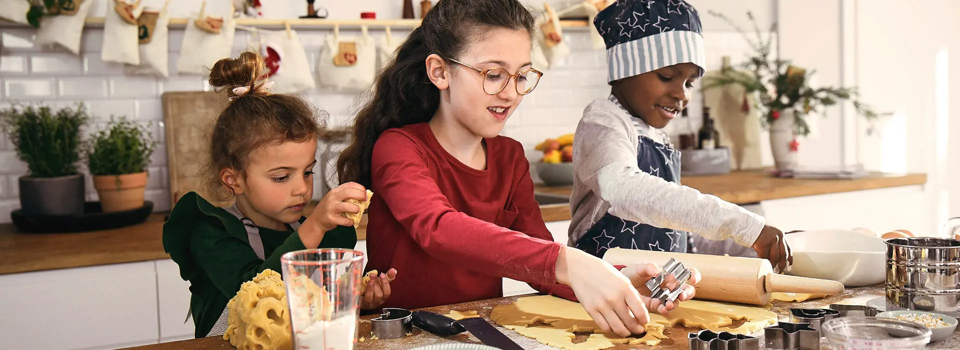 3 Kinder stechen gemeinsam Plätzchen aus.