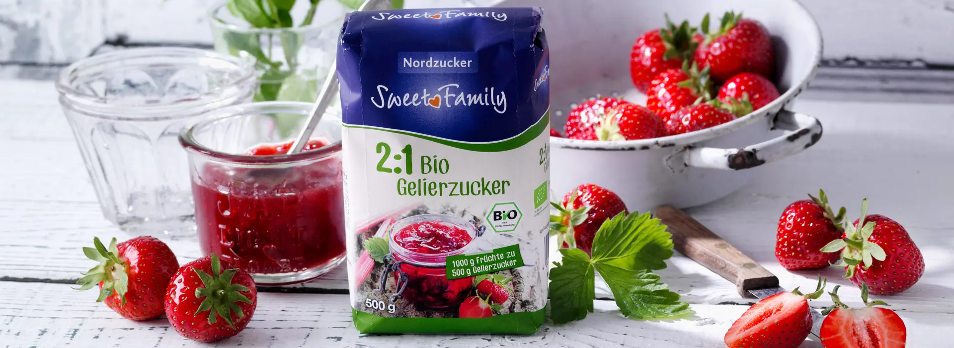 Zwei zu Eins Bio Zucker von Sweetfamily umringt von frischer Erdbeermarmelade und Früchten