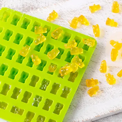 Eine knallgrüne Gummibärchenform in der viele gelbe Gummibärchen liegen
