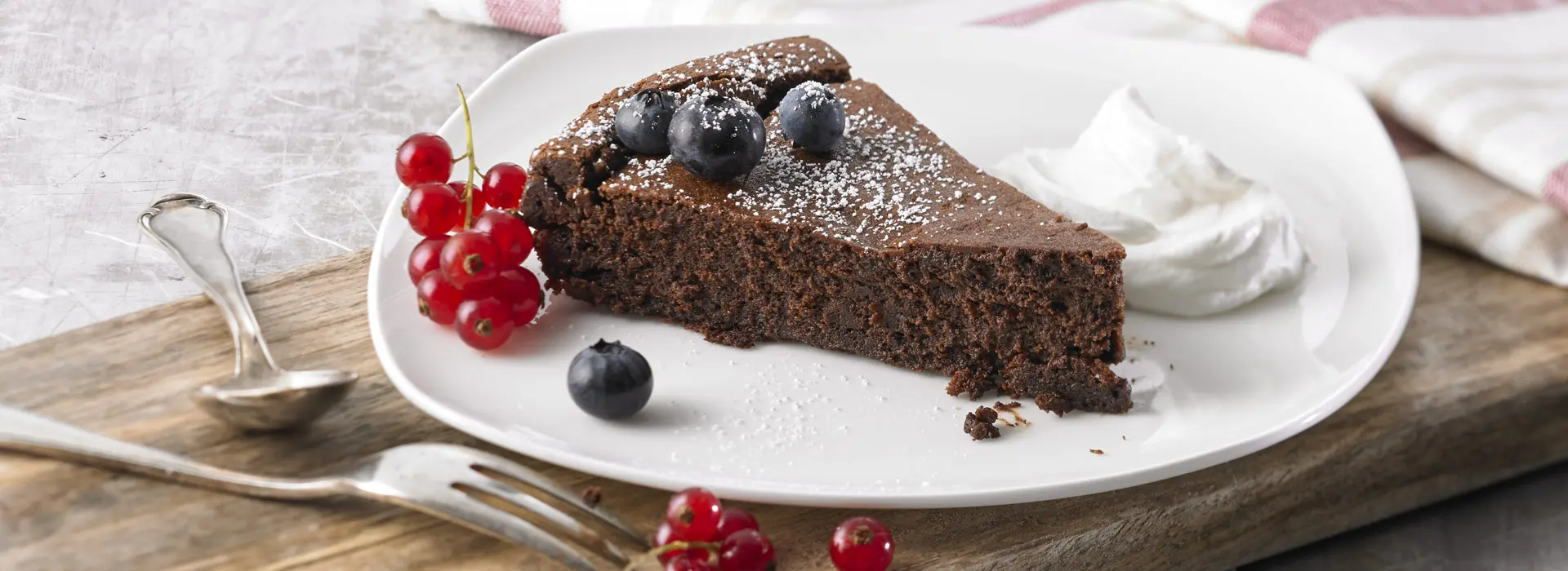 Ein saftiges Stück schokoladen Kuchen liegt auf einem Teller, neben einer kleinen Portion Shane und frischen Beeren.
