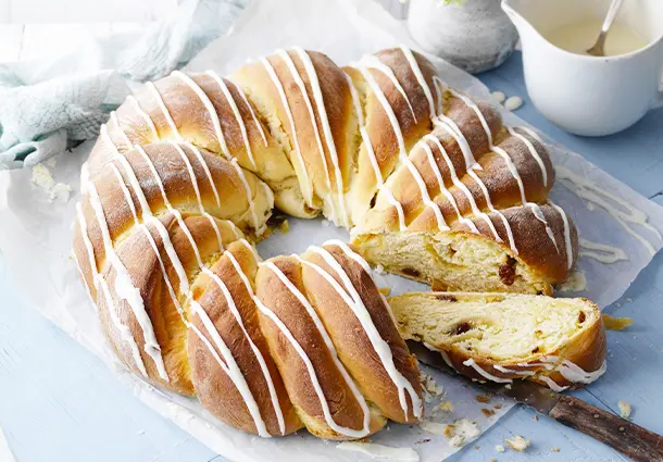 Ein großer geflochtener Hefekranz mit Marzipanfüllung ist mit weißem Zuckerguss dekoriert; ein Stück wurde zum Servieren herausgeschnitten