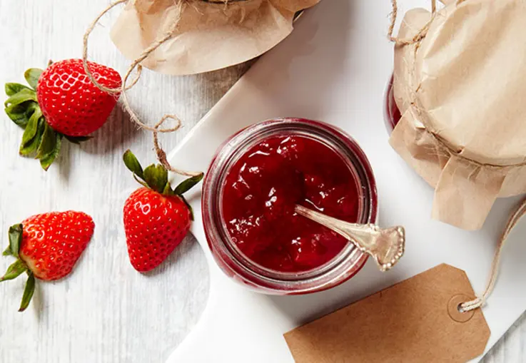 Erdbeeren umringen ein vollen Glas dunkler Erdbeermarmelade