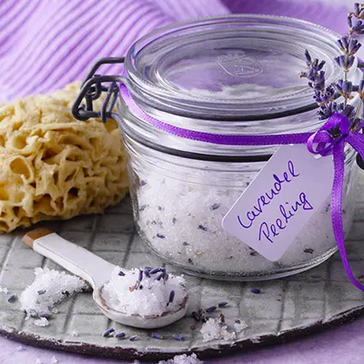 Ein Glas Lavendel‑Zucker‑Peeling ist mit violetter Schleife und getrockneten Lavendelblüten dekoriert.