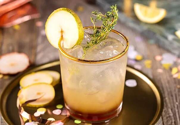 Auf einem funkelnden Tablet steht ein alkoholfreier Birnen-Tonic mit Eiswürfeln, dekoriert mit Thymian und Birnenscheiben