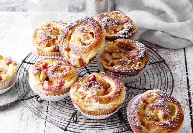 Hefeschnecken mit Rhabarberstückchen und cremiger Schmandfüllung, in Muffinformen goldbraun gebacken und mit Puderzucker bestäubt