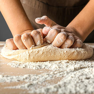 Zwei Hände kneten einen weichen Teig auf einer bemehlten Arbeitsfläche; der Fokus liegt auf der Bewegung der Finger und der Struktur des Teigs.