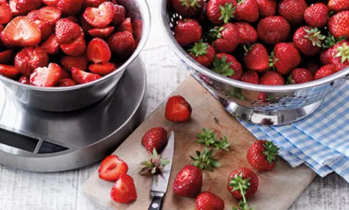 3. Früchteauswahl Eine volle Schale unbearbeiteter Erdbeeren steht neben einer großen silbernen Wage, die mit geschnittenen Erdbeeren gefüllt ist.