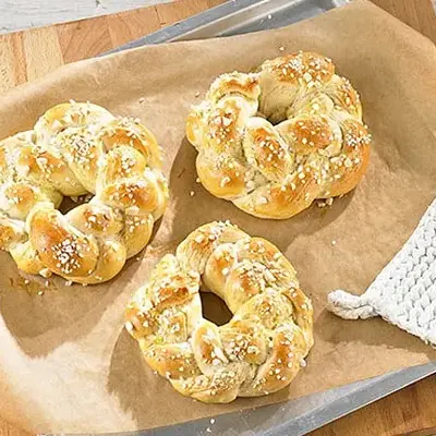 Eine kleine Platte mit geflochtenen Hefebrötchen, daneben ein Block Marzipan mit Mandeln und eine Schale Pflaumenkompott.