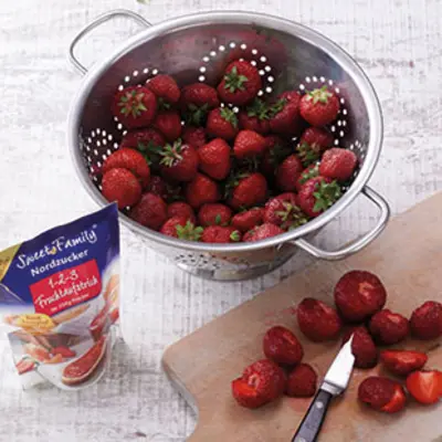 In einem großen silbernen Sieb liegen viele unbearbeitete Erdbeeren. 