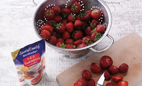 Schritt 1 Ein Sieb mit unbearbeiteten Erdbeeren. Daneben steht das Produkt 123 Fruchtaufstrich von Swéetfamily.