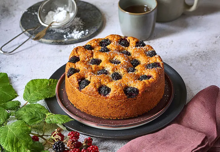 Goldbrauner Mandelkuchen mit eingebackenen Brombeeren und feiner, leicht aufgerissener Oberfläche.