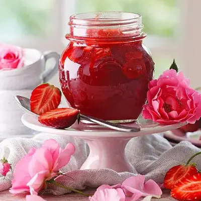 Bauchiges Glas mit roter Marmelade auf einer Tortenetagere dekoriert mit zahlreichen Rosen und Blüten