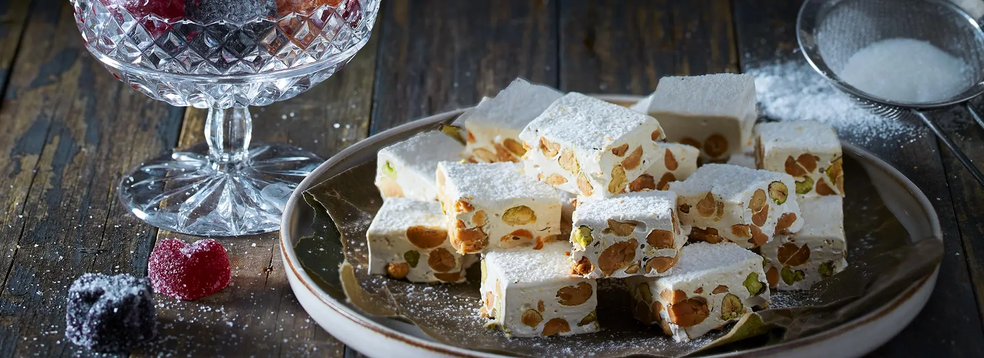 Auf einem grauen Teller sind weiße quadratische Sweets mit Nüssen aufgestapelt.