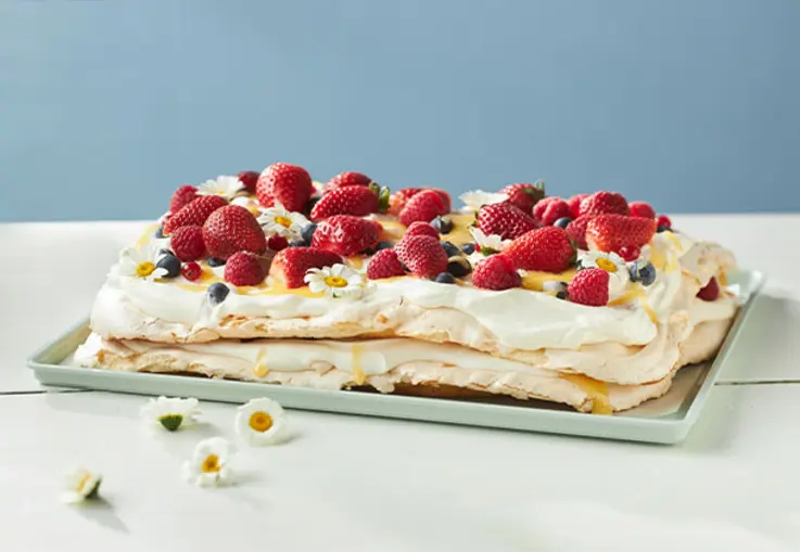 Rechteckige Baiser-Schnitten mit Lemon Curd, Sahne und frischen Erdbeeren sind mit Blüten dekoriert.